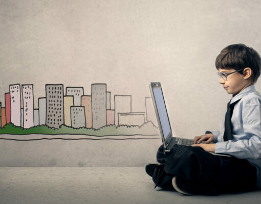 Young child sitting on the ground dressed up like a businessman and looking at his laptop